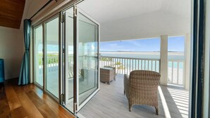 A balcony with a glass door leading to a beach view, wicker furniture, and wooden flooring. - Oceanfront mansion, heated infinity pool. 6 double rooms, 11 beds can sleep 18 (George Town)