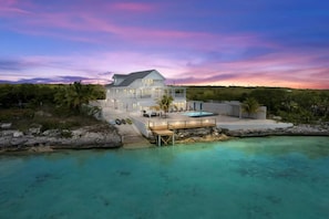 A large, modern house with a pool, surrounded by tropical vegetation and a clear blue sea.