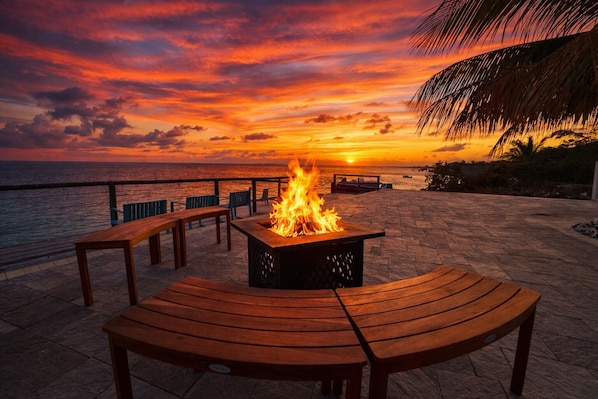 A fire pit with a sunset view, wooden benches, and a paved deck.