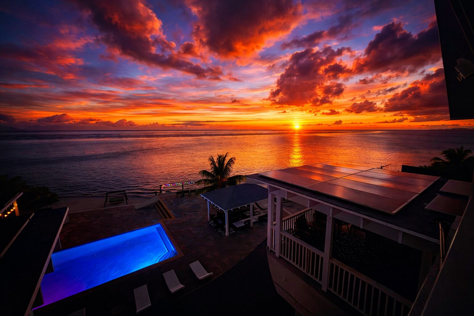 A sunset view from a rooftop pool area with lounge chairs and a small covered seating area.