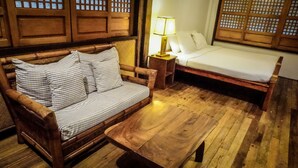 Een houten bank met gestreepte kussens, een houten tafel en een bed met wit beddengoed.