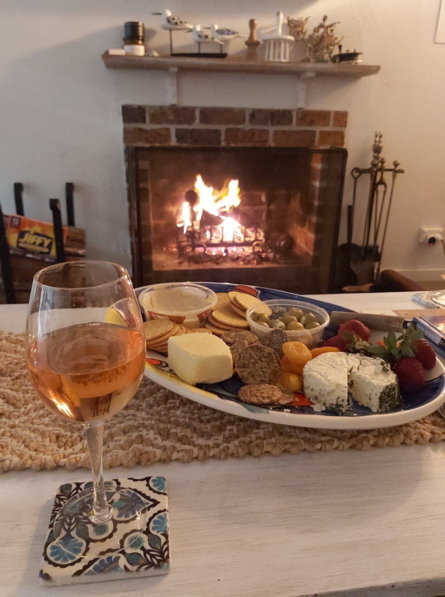 A plate of assorted cheeses and crackers on a table with a glass of wine, in front of a fireplace.