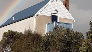 Un bâtiment à l’extérieur blanc, avec une porte bleue, entouré de verdure.