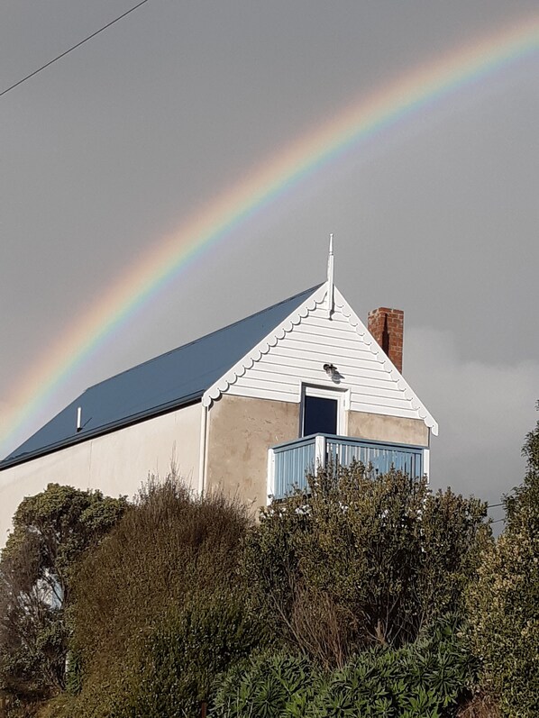 Un bâtiment à l’extérieur blanc, avec une porte bleue, entouré de verdure.