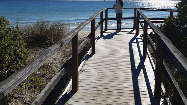 Une promenade en bois qui mène à une plage, avec un ciel bleu dégagé.