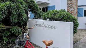 Un vélo rouge est garé devant un immeuble sur lequel on peut lire l’inscription « Sandpiper ».