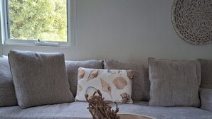 Un salon comprenant un canapé, un vase décoratif, un tableau encadré et une fenêtre donnant sur des arbres.