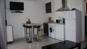Cocina compacta con lavadora, cafetera y televisor montado en la pared.