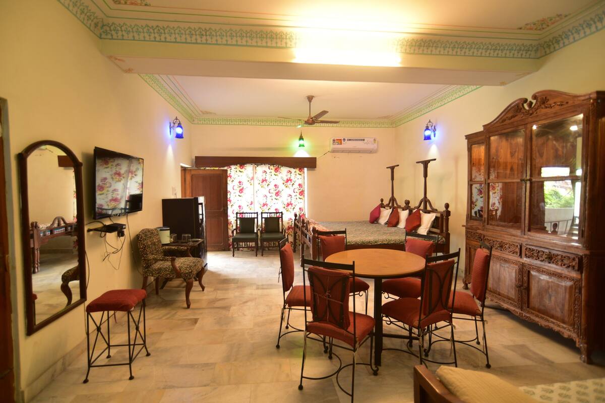 A dining area with a round table and chairs, a mirror, a television, and a cabinet.