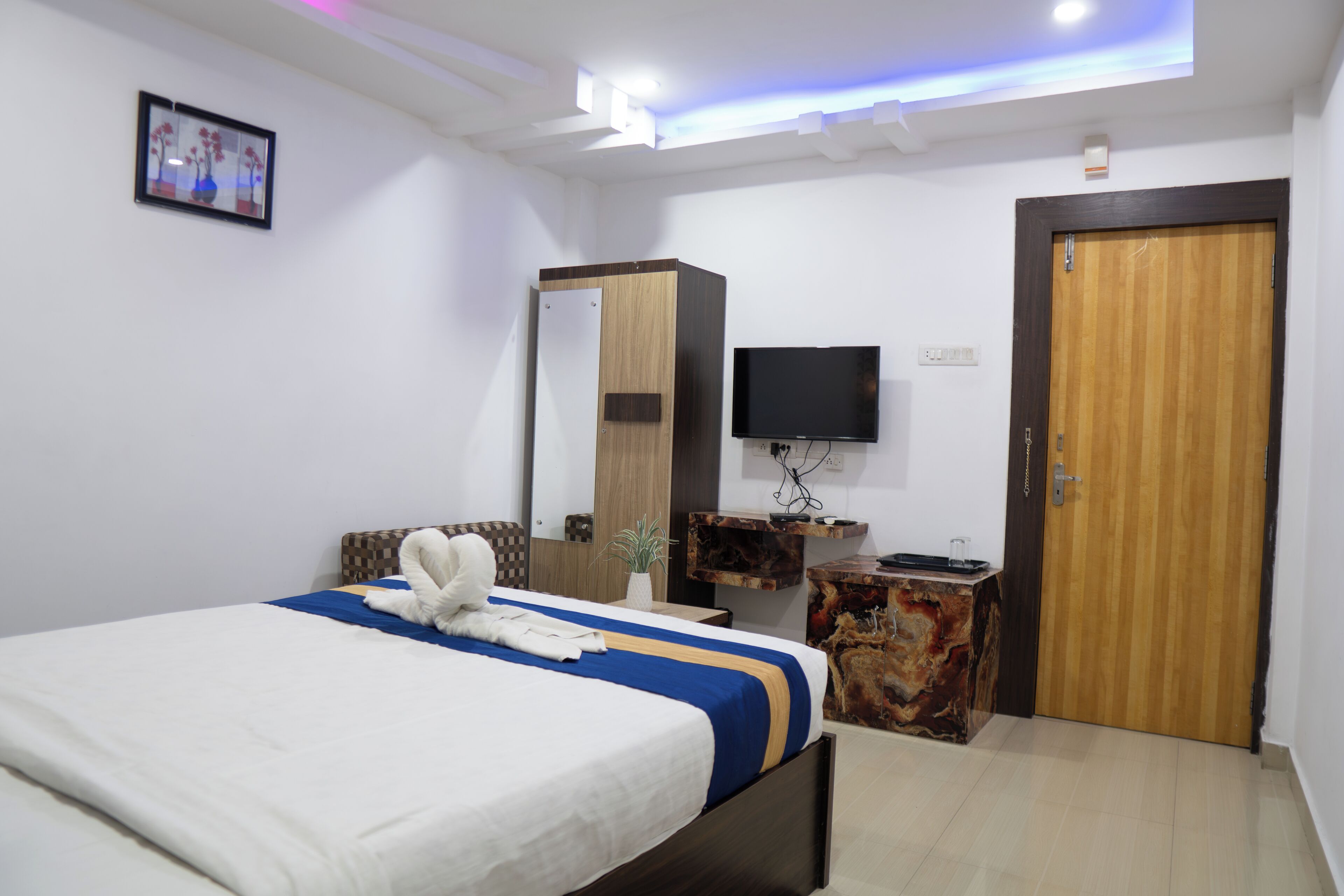 Una habitación de hotel moderna con cama, televisión de pantalla plana, puerta de madera y una mesita con un florero.