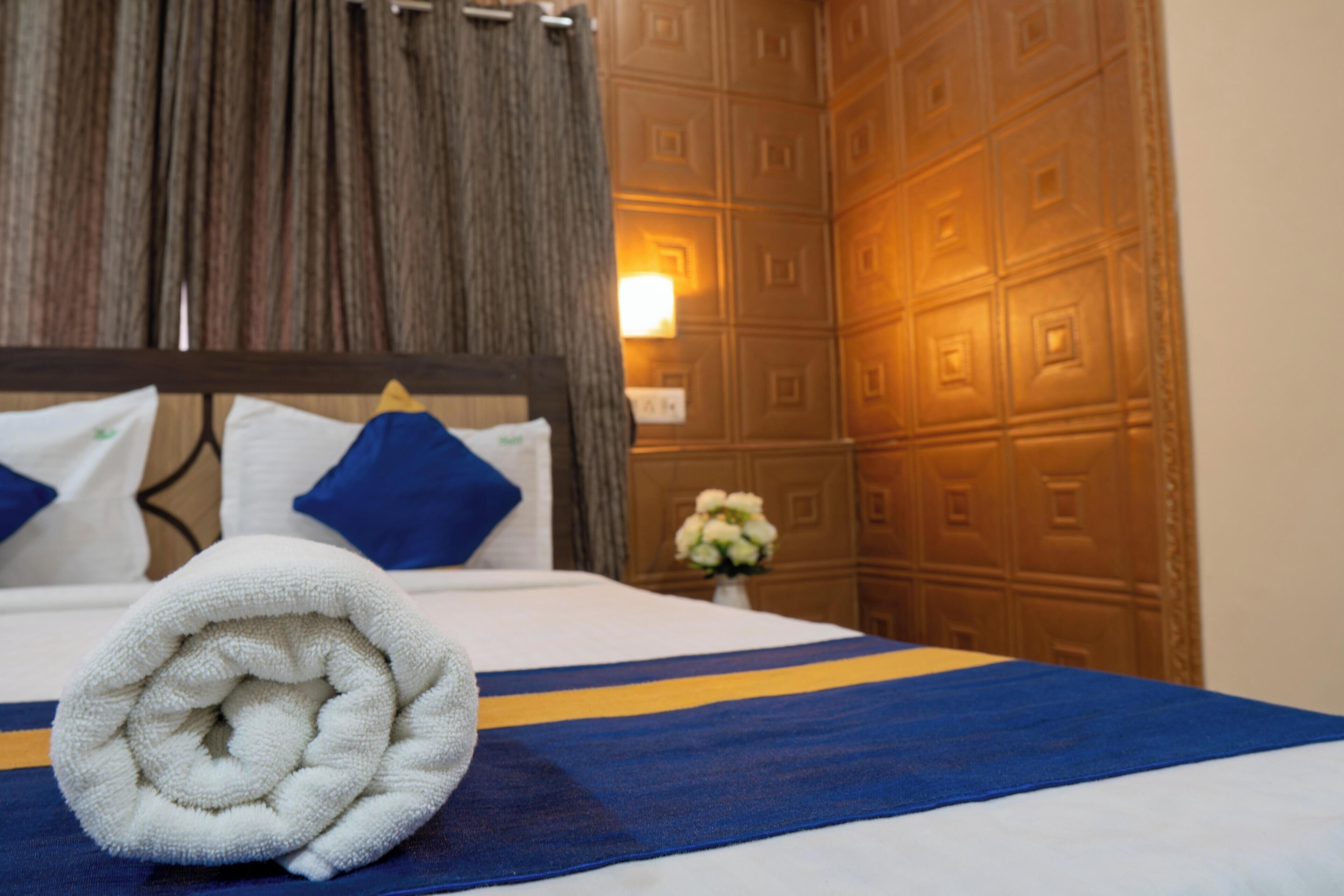A neatly made bed with a rolled white towel, blue and yellow striped bedspread, and blue pillows.