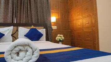 A neatly made bed with a rolled white towel, blue and yellow striped bedspread, and blue pillows.