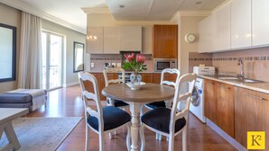 A modern kitchen with white cabinets, a wooden dining table, and a built-in washing machine. - Unit 613 Cape Royale Apartments (Cape Town)