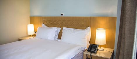 A hotel room with a neatly made bed, two bedside lamps, a bedside phone, and a wooden headboard.