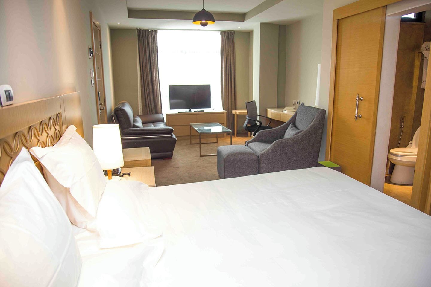 A hotel room with a large bed, a sofa, a chair, a TV, and a desk.