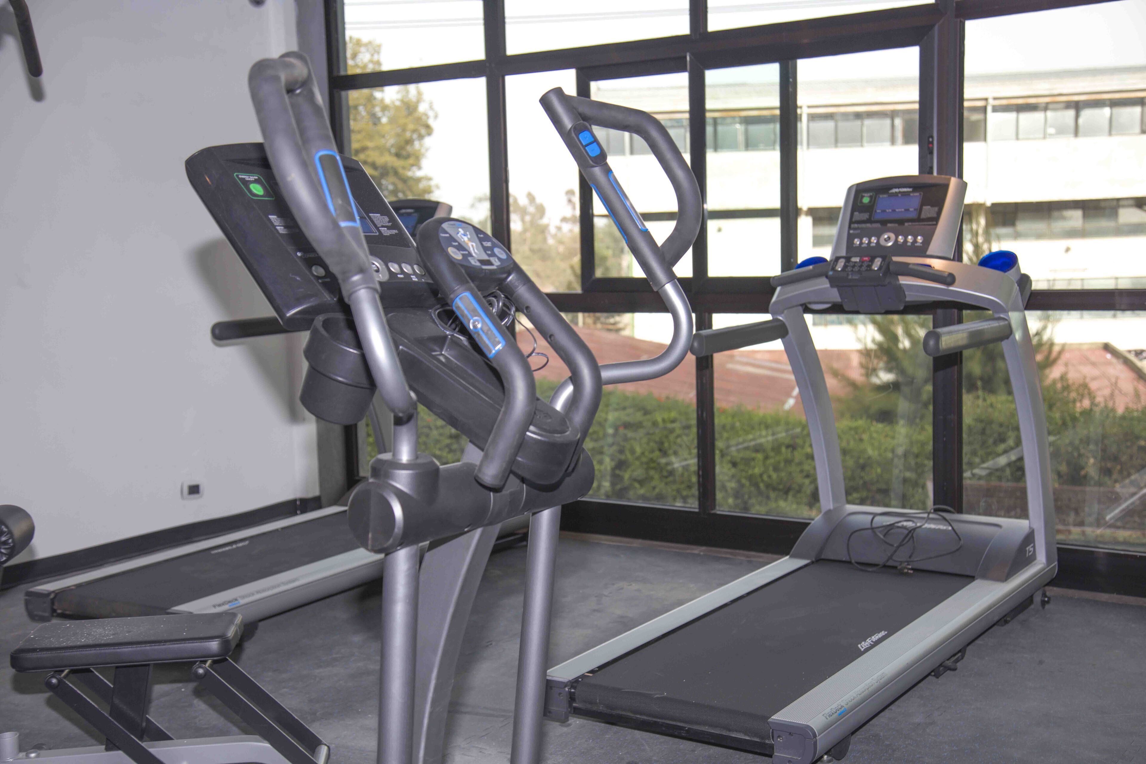 Dos máquinas de ejercicio en una sala con ventanas amplias.