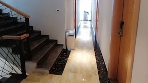 A hallway with a marble floor, a staircase with wooden handrails, and a door with a handle.