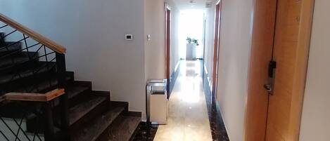 A hallway with a marble floor, a staircase with wooden handrails, and a door with a handle.