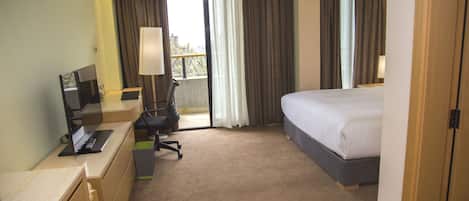 Habitación de hotel con cama, escritorio, laptop, una silla y ventana con cortinas.