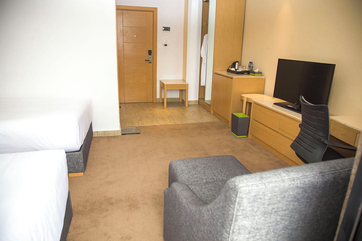 A hotel room with two single beds, a small desk with a chair, a television, and a trash bin.
