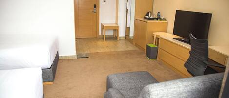 A hotel room with two single beds, a small desk with a chair, a television, and a trash bin.