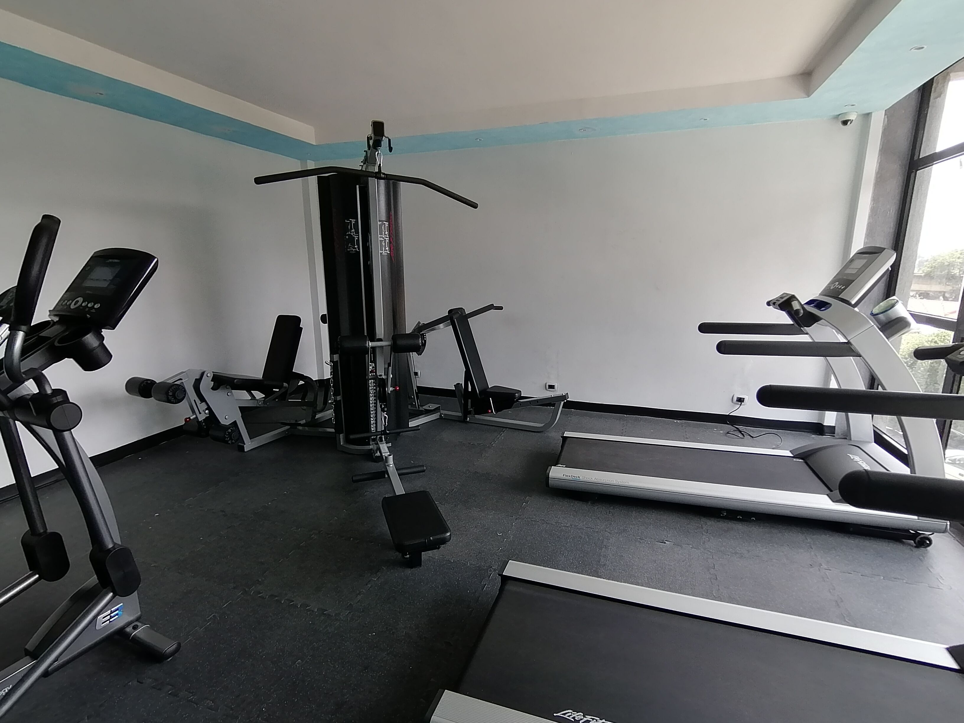 Ein Fitnessraum mit Cardiogeräten, Krafttrainingsgeräten und einem Laufband.