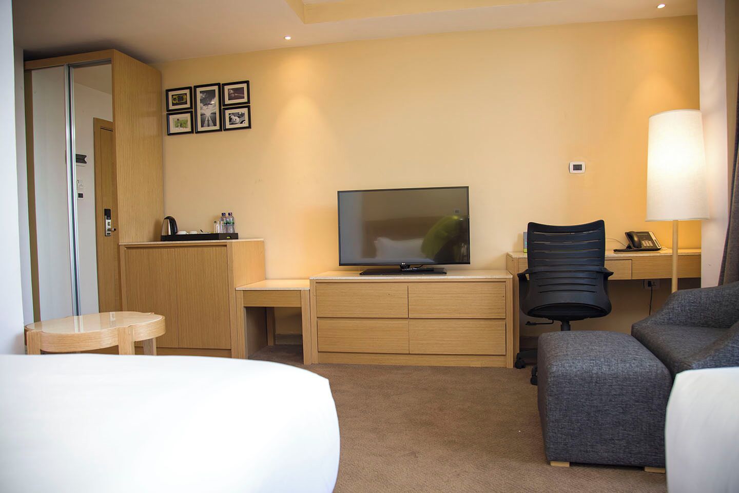 Habitación de hotel con cama, escritorio con televisor, silla, lámpara y armario.