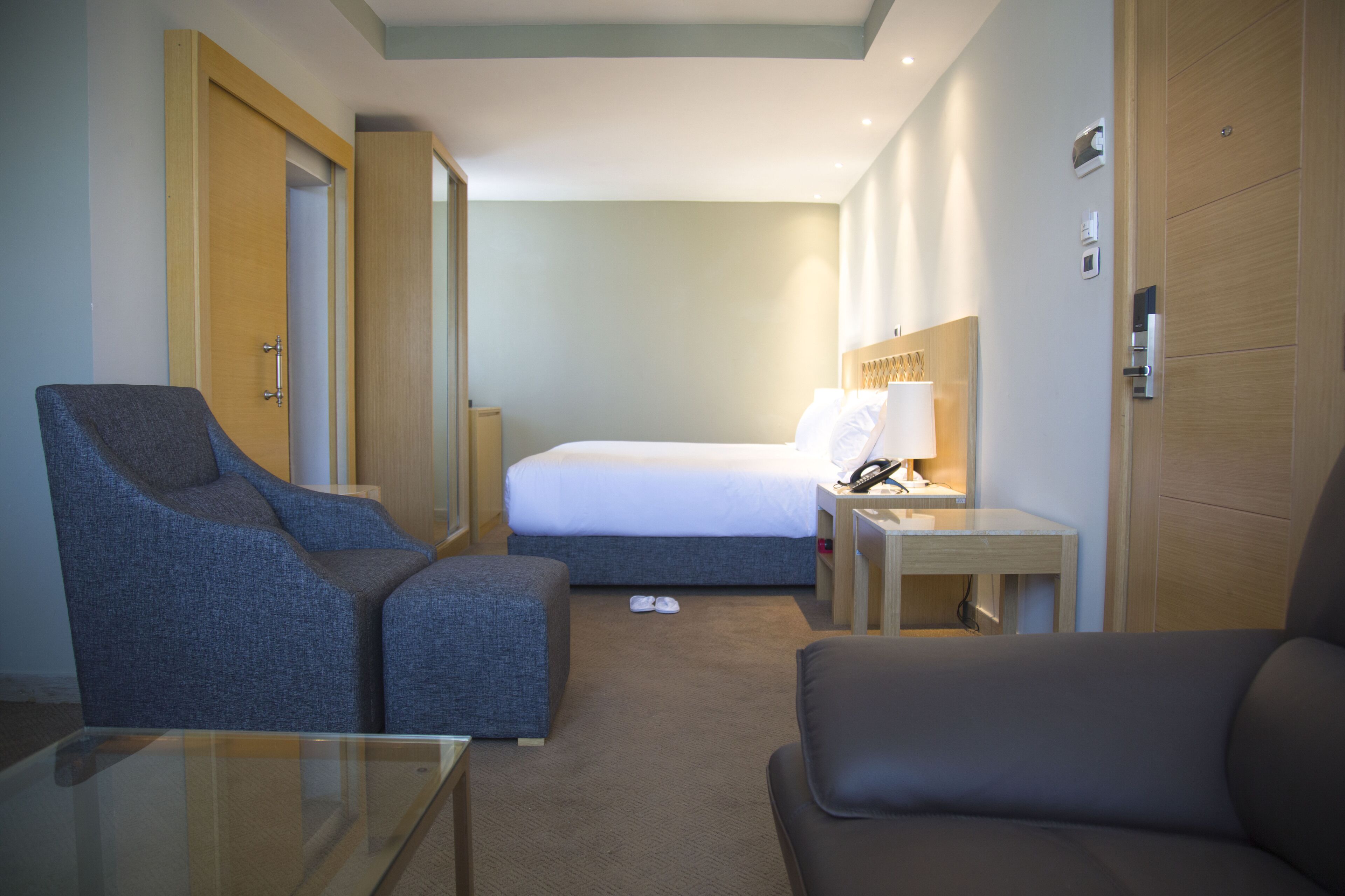 A hotel room with a bed, a desk with a lamp, a chair, and a sofa.