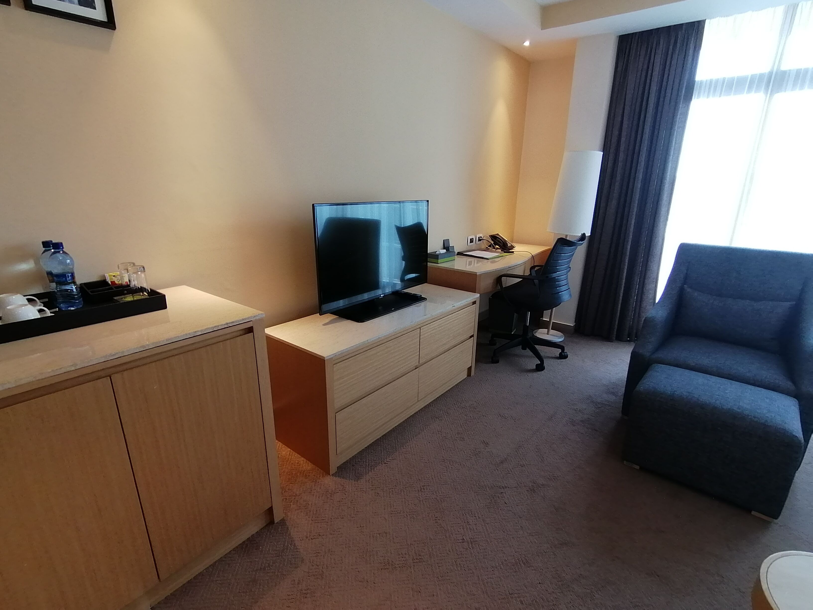 A hotel room with a desk, a television, a chair, and a sofa.