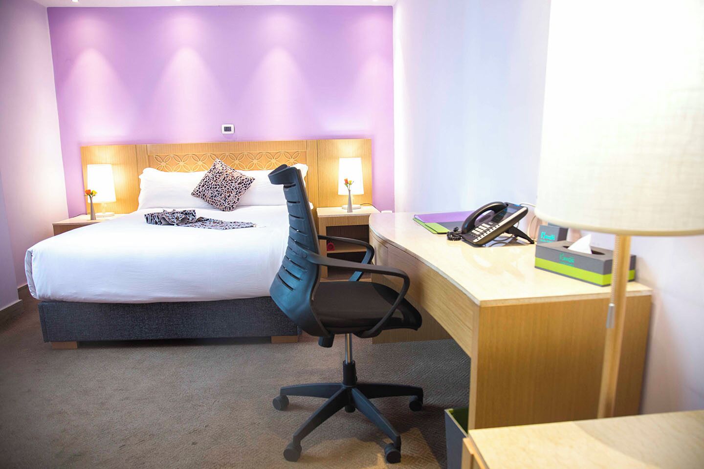Habitación de hotel con una cama, un escritorio con teléfono y una lámpara, y una silla.