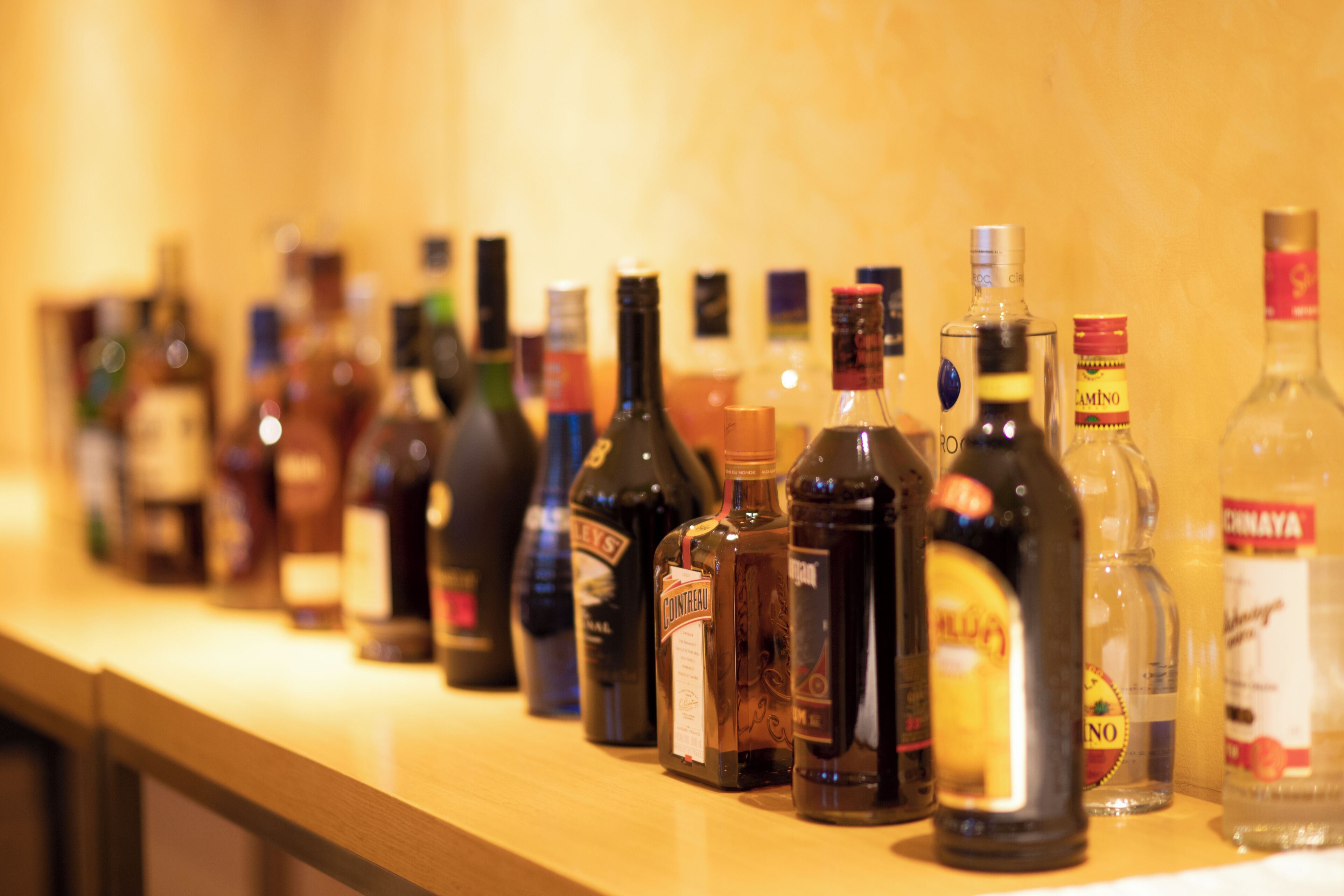 A variety of liquor bottles lined up on a wooden shelf.