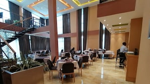 A spacious dining area with multiple tables and chairs, a staircase, and a reception desk.