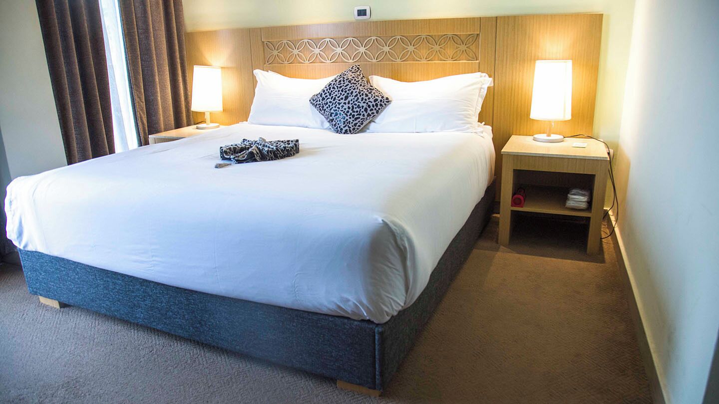 A hotel room with a large bed, two bedside lamps, a nightstand with a lamp, and a small shelf.