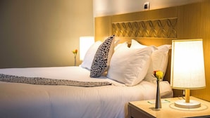 A hotel room with a neatly made bed, a bedside lamp, and a decorative wall panel.