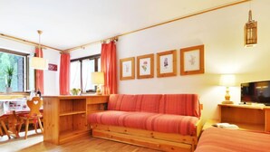 Una habitación acogedora con un sofá de madera, televisión, escritorio con silla y cuadros en la pared.