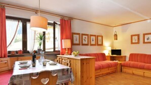 Una sala de estar acogedora con un sofá de madera, una mesa de comedor con sillas y una zona de cocina.