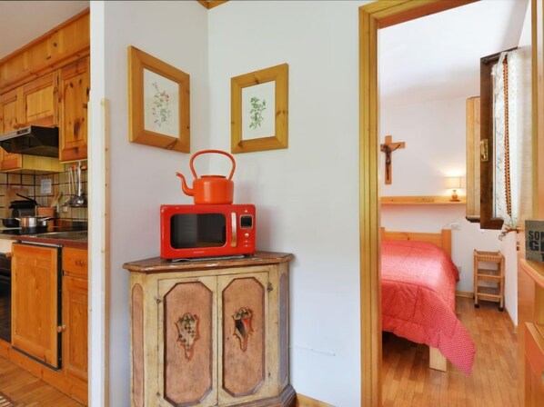 A compact kitchen with wooden cabinets, a red microwave, and a small cabinet with decorative carvings. - Apartment Apt 3 by Interhome (Canazei)