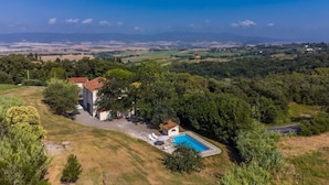 A villa with a swimming pool, surrounded by lush greenery and a view of distant hills. - Lovely apartment in villa for 10 guests with pool, TV and pets allowed (Rosignano Marittimo)