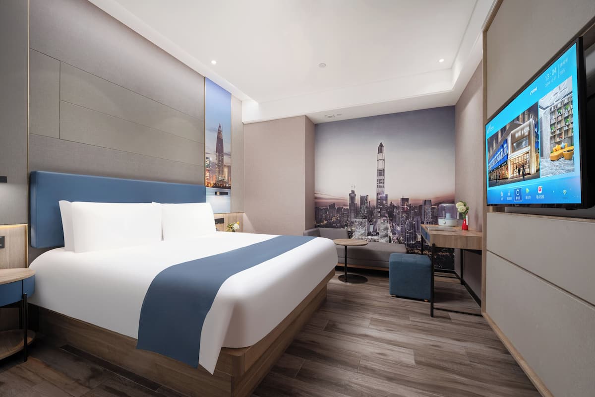 A modern hotel room with a large bed, a desk, and a TV displaying a cityscape.