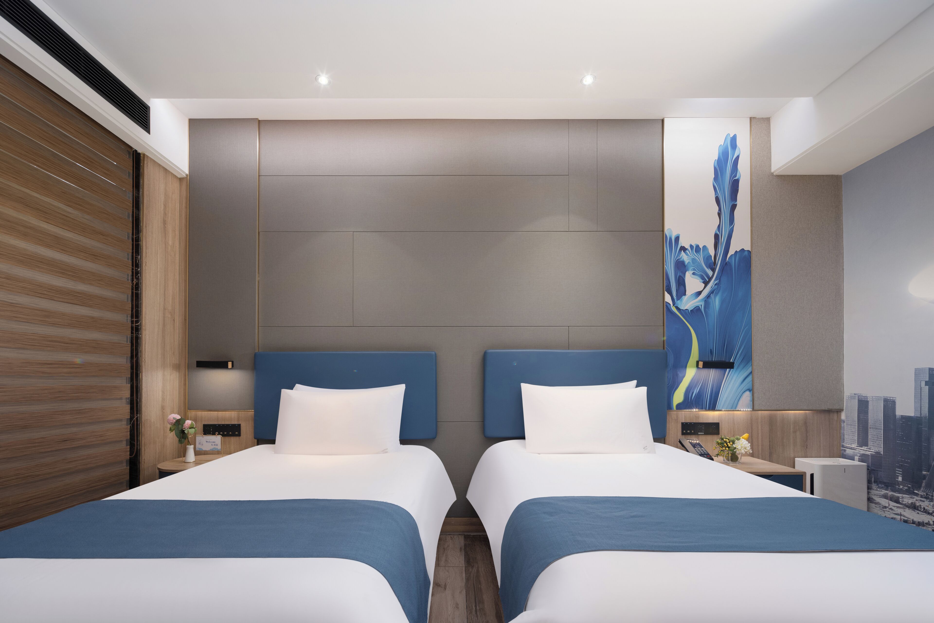 Quarto de hotel moderno com duas camas, um mural com vista para a cidade e painel de parede de madeira.