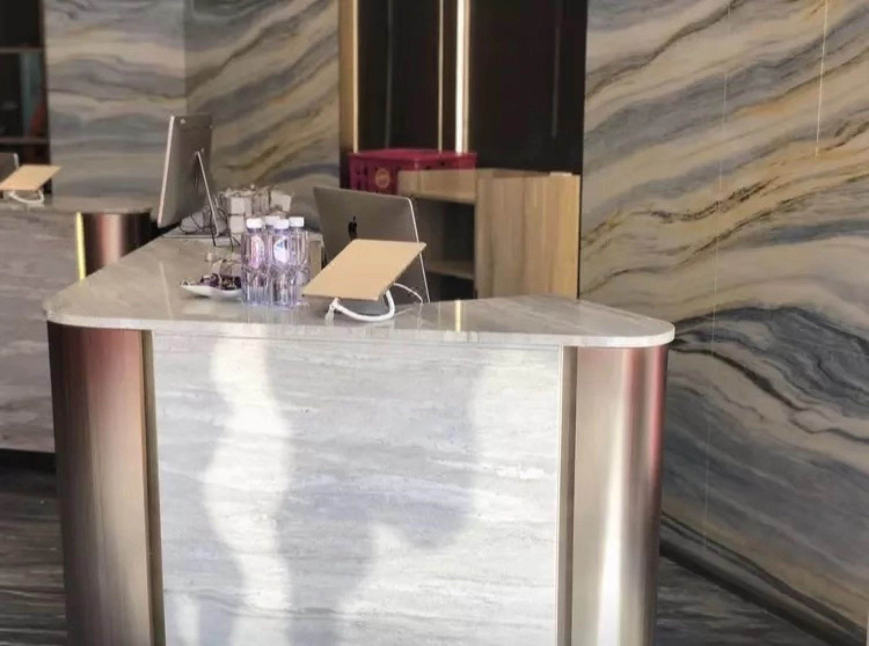 A reception desk with a marble countertop, a laptop, and a glass of water.