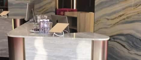 A reception desk with a marble countertop, a laptop, and a glass of water.