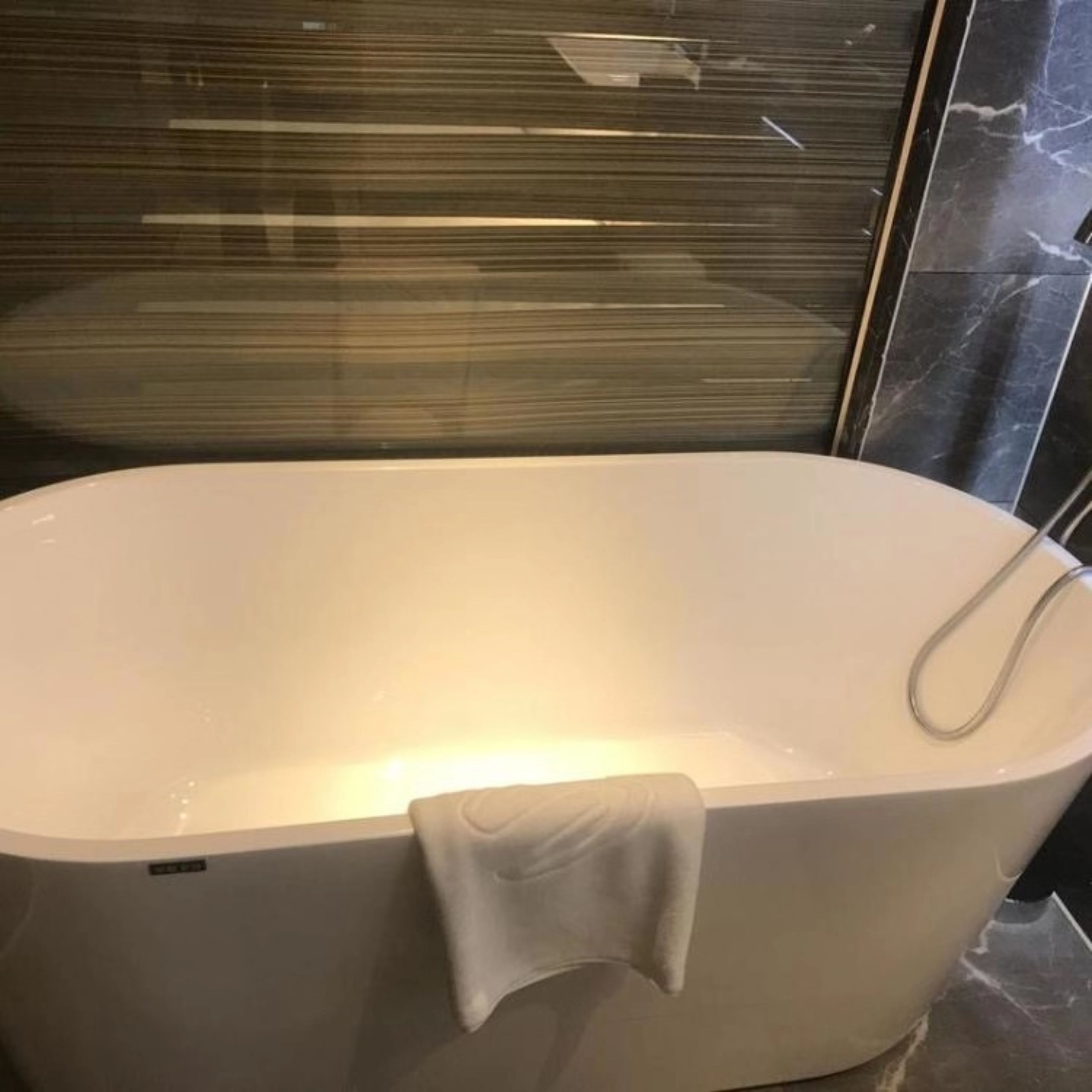 Una bañera moderna con un cabezal de ducha manual, frente a una pared de mármol oscuro.