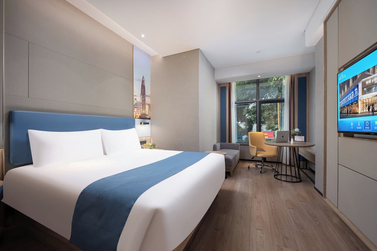 A modern hotel room with a large bed, a desk with a chair, and a TV on the wall.