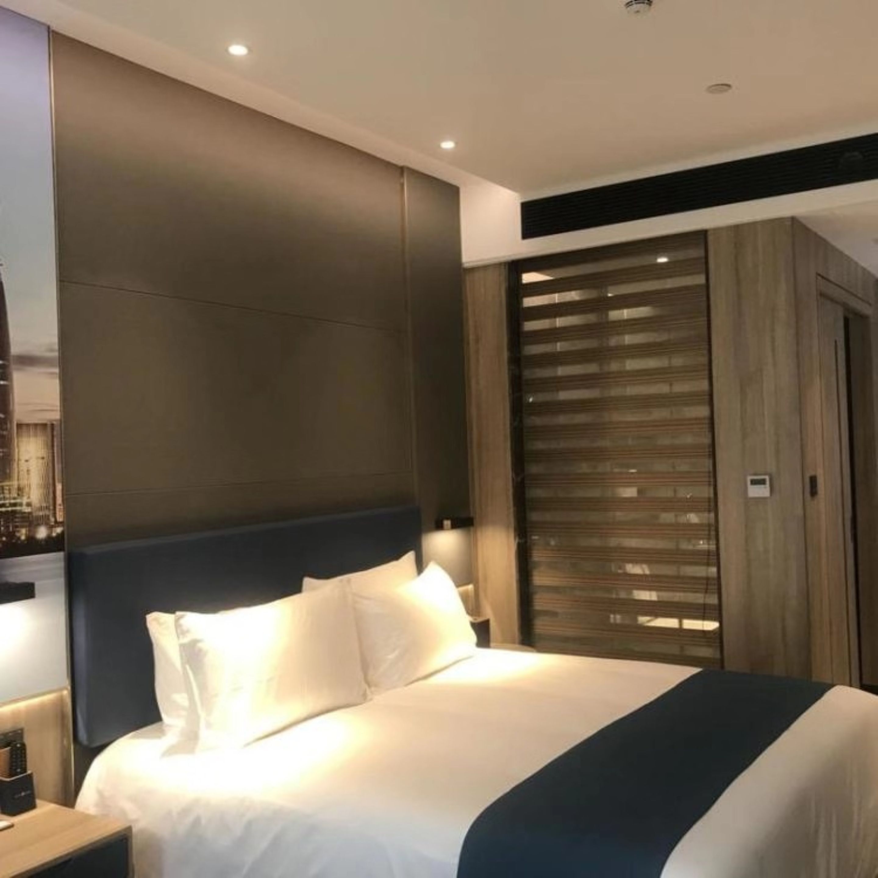 Una habitación de hotel moderna con una cama grande, un armario de madera y una mesita de noche con una lámpara.
