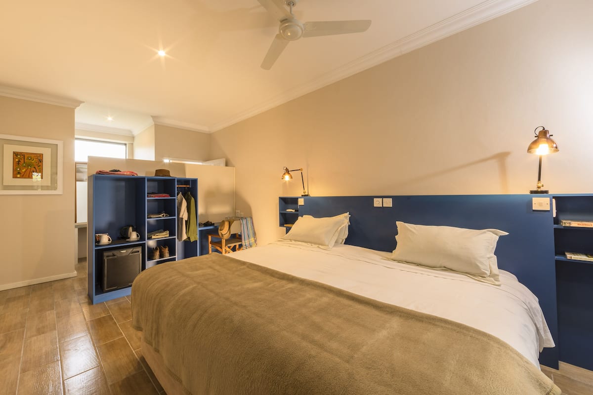 A bedroom with a bed, a ceiling fan, a desk with a lamp, and a wardrobe.