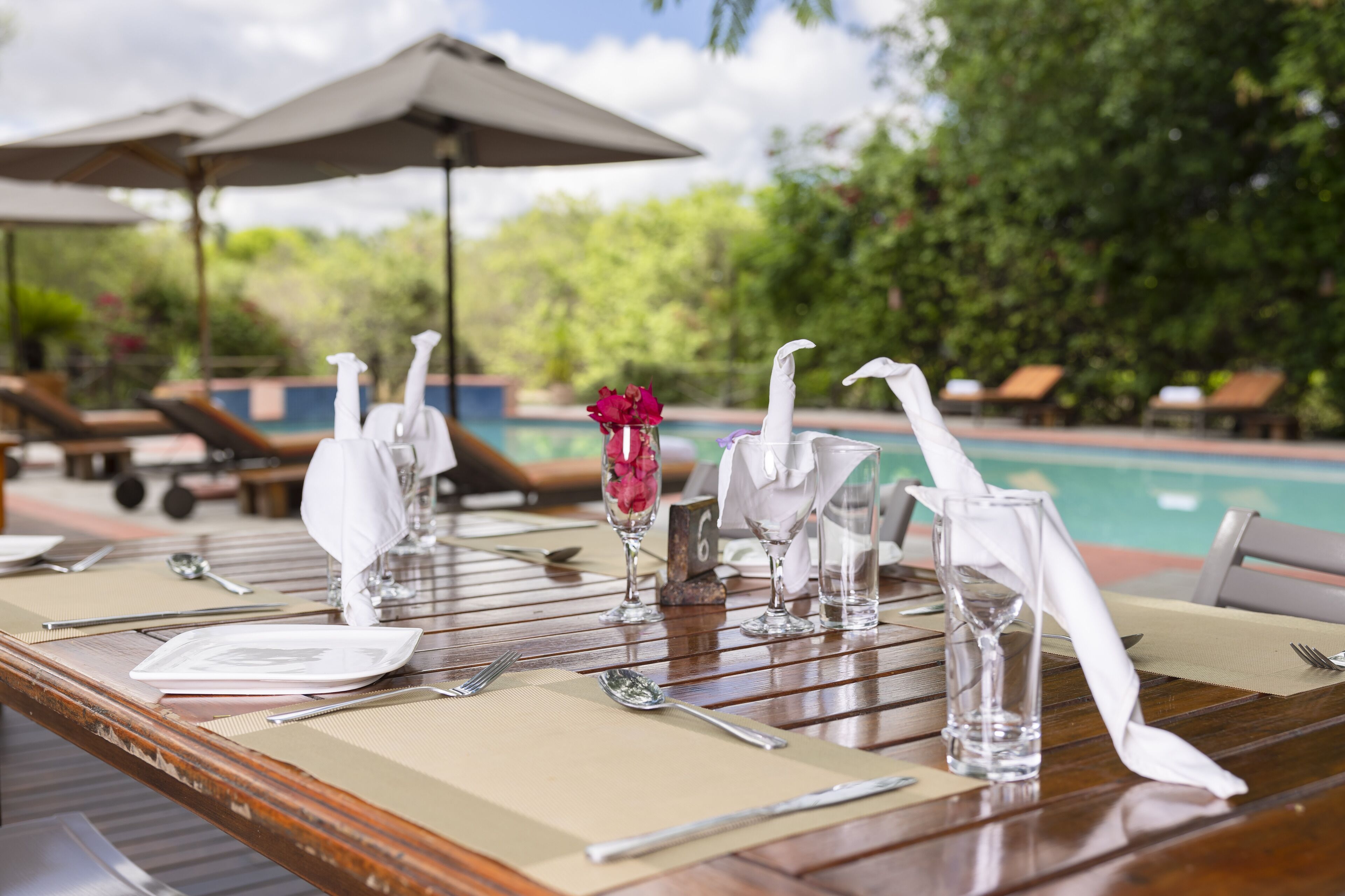 A dining table set with white napkins, silverware, and a small vase with pink flowers.
