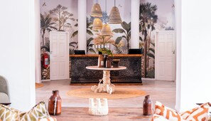 A lobby with a reception desk, a round table with decorative items, and a mural of tropical foliage.