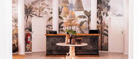 Un hall d’entrée avec une table ronde, un comptoir d’accueil et un mur recouvert d’un papier peint aux motifs tropicaux.