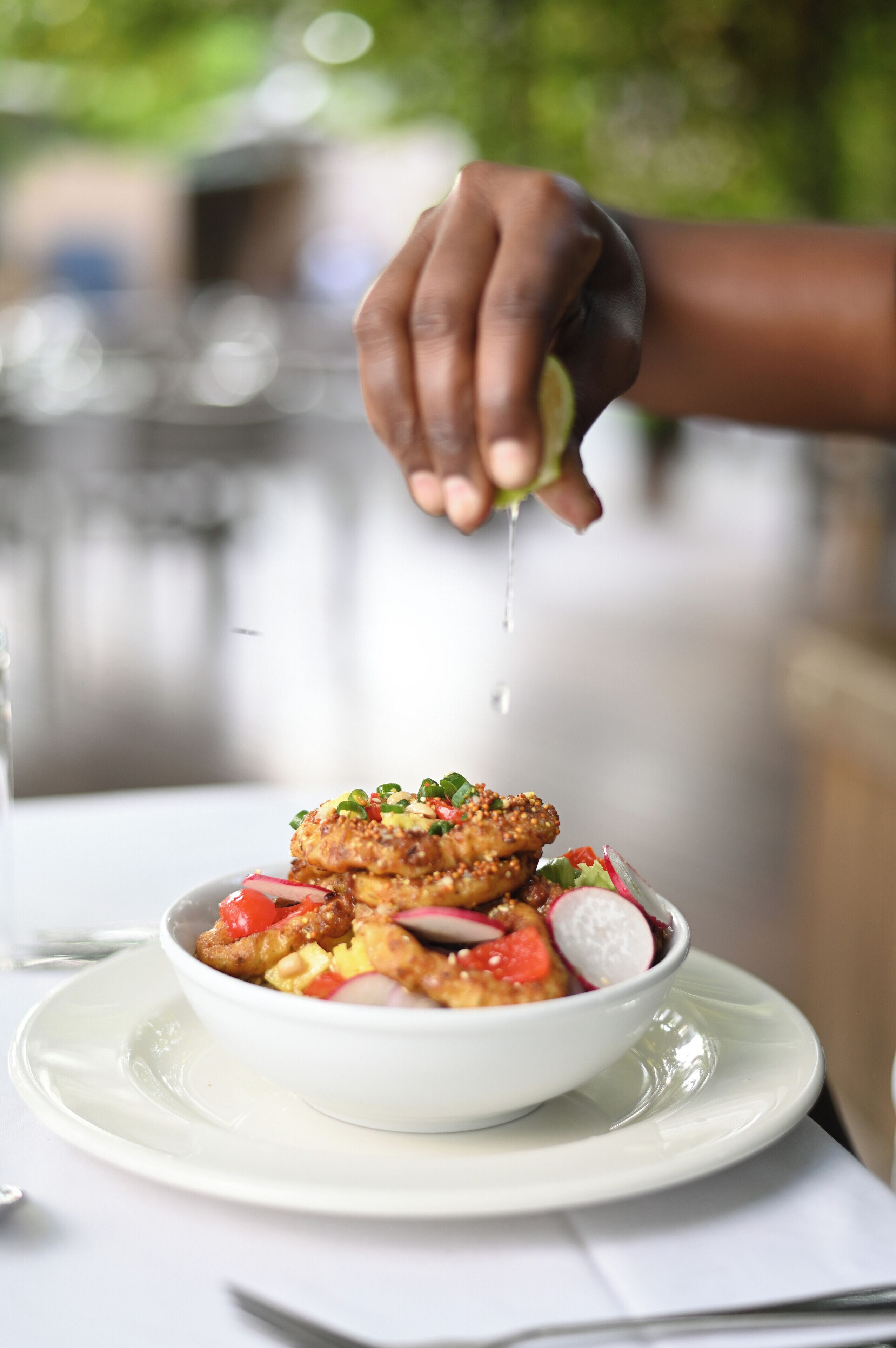 A bowl of food on a white plate with a hand squeezing a lemon over it.